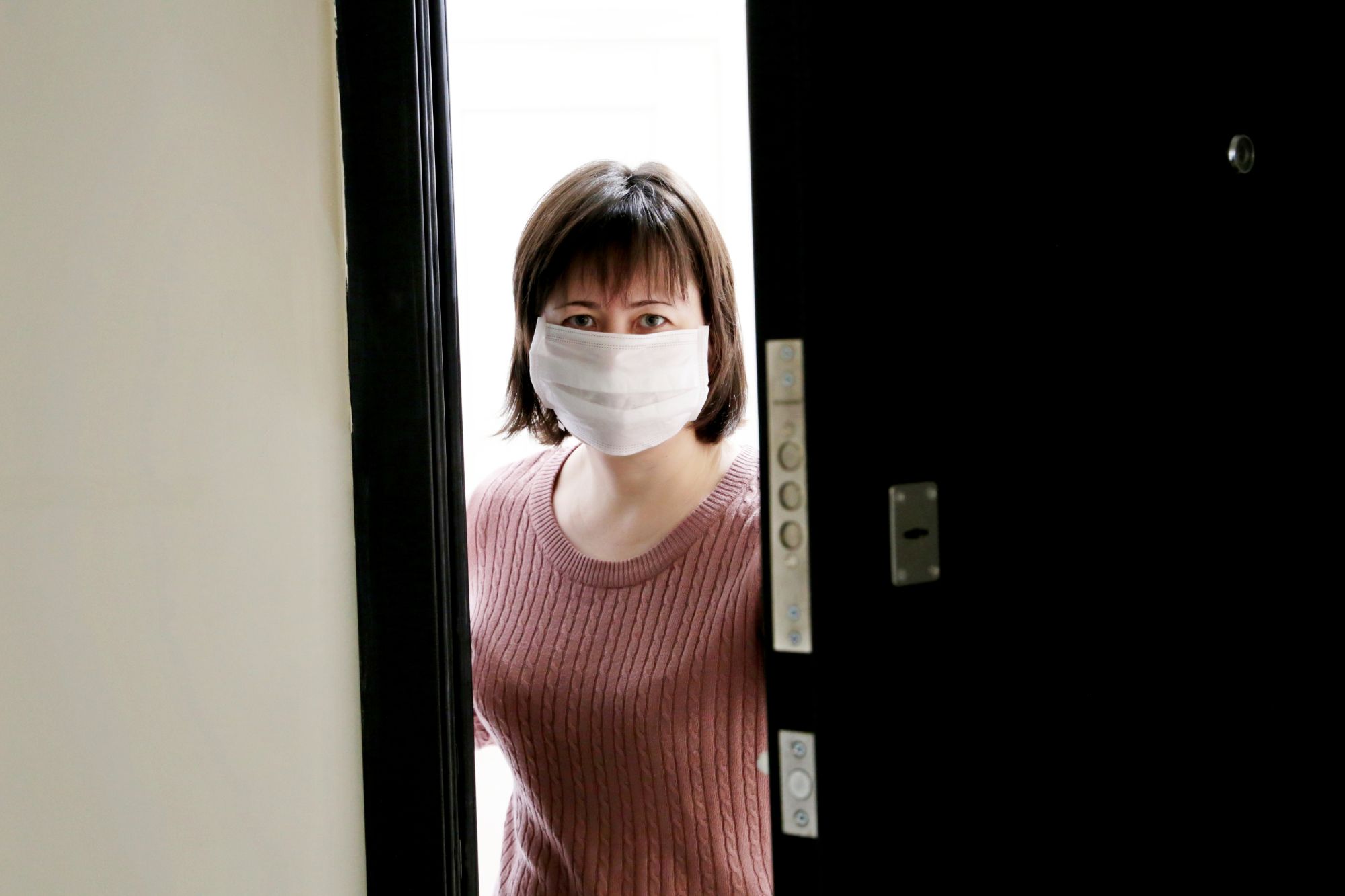 Worried woman in a medical mask standing in the open doorway